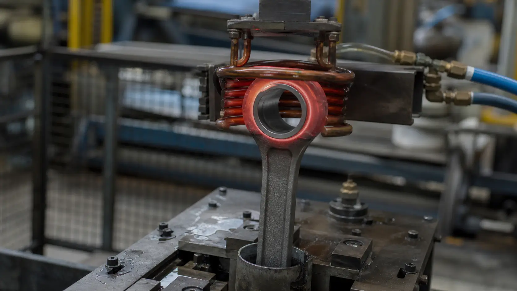 induction heating connecting rods — copper coil heating the small-end bore of a steel connecting rod in a production fixture